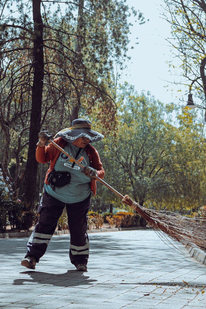 A dedicated worker cleans a park path in Ciudad de México, showcasing urban maintenance.