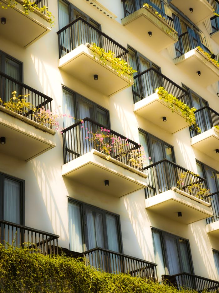 A modern apartment building facade with lush balconies in bright sunlight showcasing urban living.